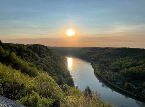Sunset over a winding river, surrounded by lush green hills and a clear sky.