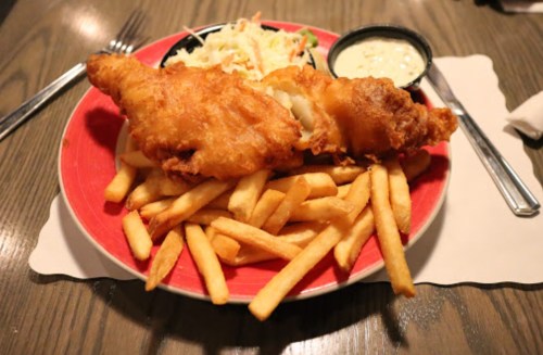 A plate of golden fried fish fillets served with French fries, coleslaw, and dipping sauce.