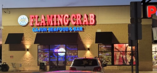 Exterior of Flaming Crab Cajun Seafood & Bar at dusk, featuring bright signage and large windows.
