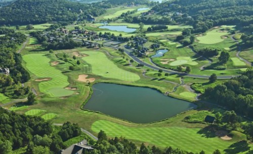 Aerial view of a lush golf course with multiple greens, water features, and surrounding trees.
