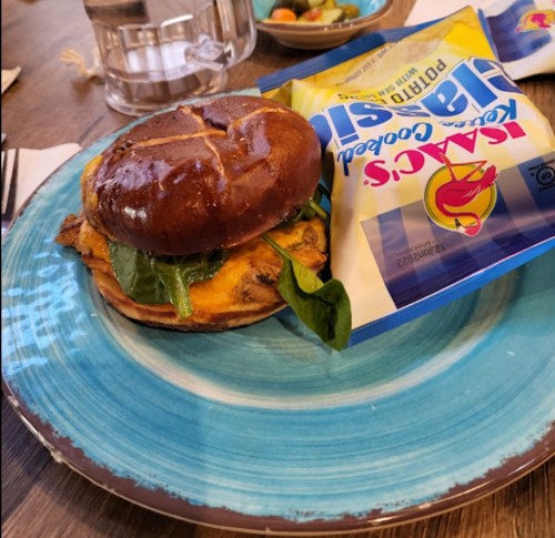 A burger with spinach on a blue plate, next to a bag of potato chips and a glass of water.