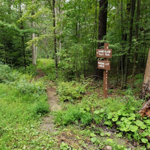 A wooded trail with a sign indicating the Bound Island Trail and parking lot area, surrounded by lush greenery.