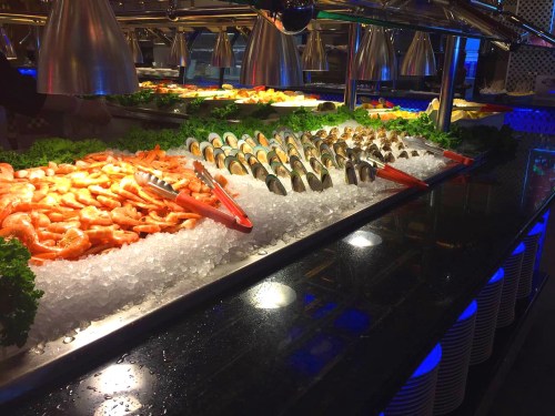 A seafood display featuring shrimp, clams, and mussels on ice, garnished with lettuce in a well-lit setting.