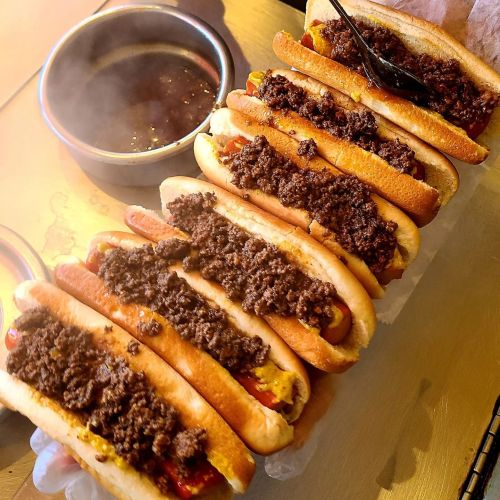 A row of hot dogs topped with ground beef, served with a side of barbecue sauce.