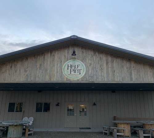 Exterior of Half Pint Brewing Co. building with wooden siding and a circular logo, under a cloudy sky.