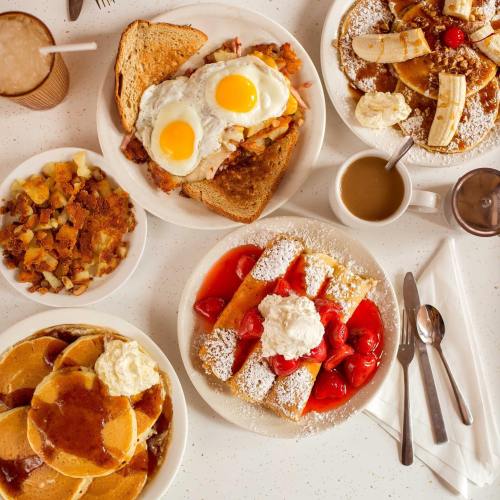 A spread of breakfast dishes including pancakes, eggs, fruit, and coffee on a table.