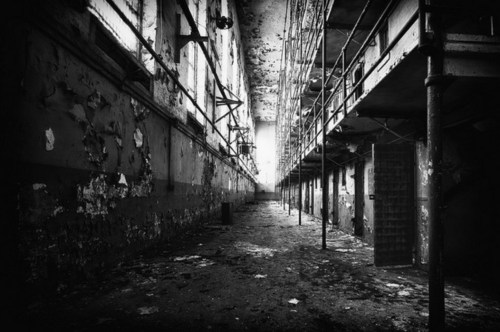 A dimly lit, abandoned corridor in a dilapidated building, featuring peeling walls and metal scaffolding.