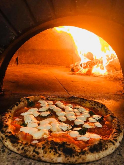 A freshly baked pizza with mozzarella sits in front of a wood-fired oven, glowing with flames.