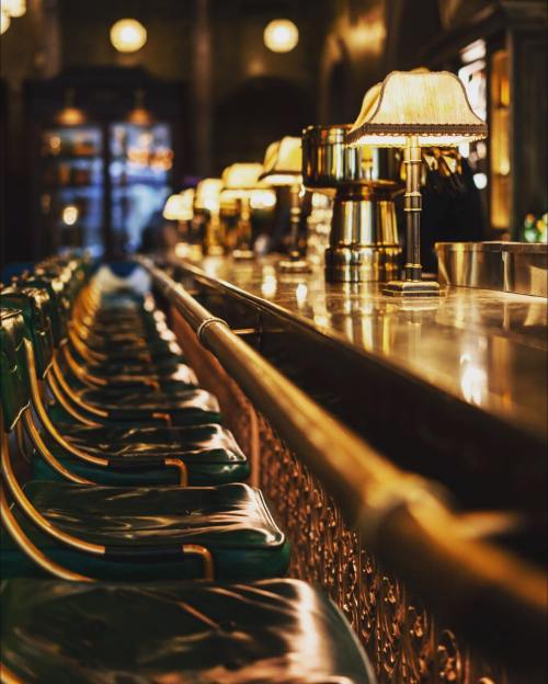 A dimly lit bar with green upholstered stools and vintage lamps lining the counter.