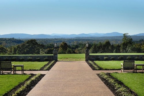 A scenic view of rolling hills and mountains, framed by a pathway and benches in a lush green landscape.
