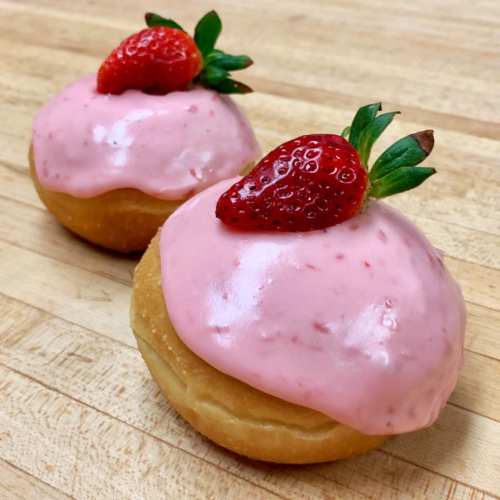 Two donuts with pink frosting topped with fresh strawberries, placed on a wooden surface.
