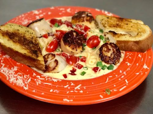 A vibrant plate of pasta with scallops, cherry tomatoes, green onions, and garlic toast, garnished with cheese.