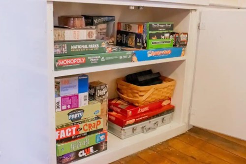 A shelf filled with various board games and a basket, including Monopoly, Clue, and National Parks.
