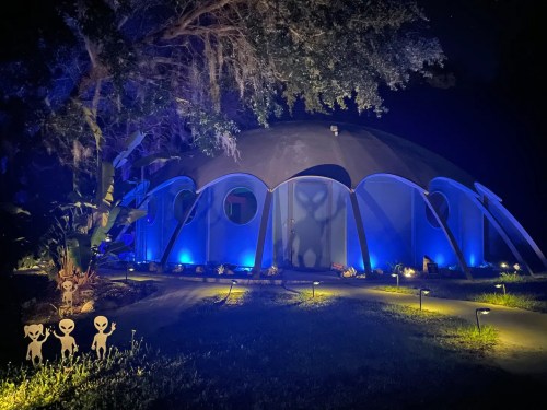 A futuristic dome structure illuminated in blue light at night, with playful alien silhouettes in the foreground.