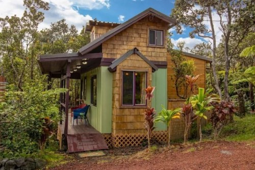 A charming, small house with a wooden exterior, surrounded by lush greenery and colorful plants.