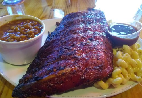 A plate featuring a large smoked rib, macaroni, and a side of baked beans with barbecue sauce.