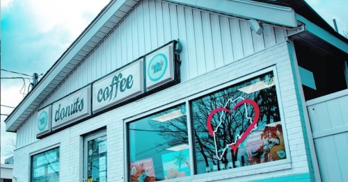 A coffee shop with a white exterior and a heart-shaped reflection in the window, surrounded by trees.