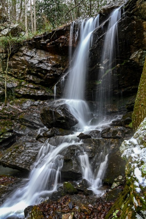 A serene waterfall cascading over rocky terrain, surrounded by lush greenery and moss-covered stones.