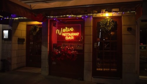 A warmly lit restaurant bar entrance with a glowing neon sign reading "Veuve Restaurant Bar" and festive decorations.