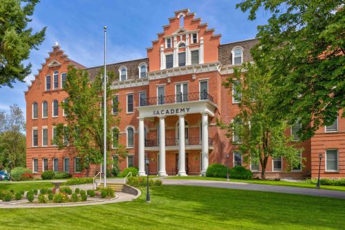 Historic brick building with a decorative facade, surrounded by green lawns and trees, labeled "Academy."