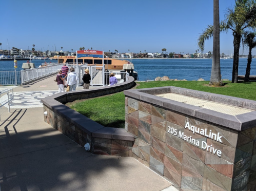 AquaLink sign at a marina with a docked boat, palm trees, and people walking along the waterfront.