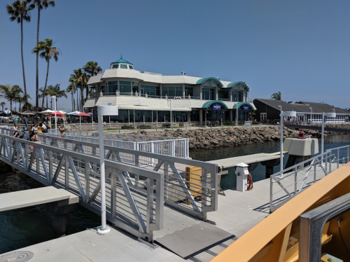 A waterfront building with palm trees, a dock, and people enjoying the sunny day by the water.