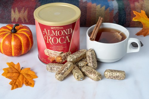 A can of Almond Roca, a cup of tea, and chocolate-covered candies arranged with autumn leaves and a pumpkin.