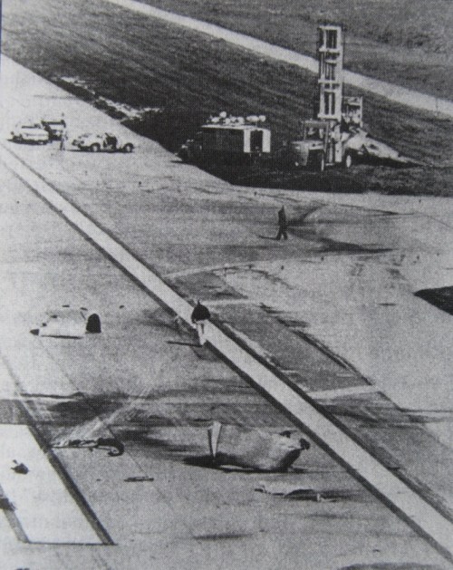 Aerial view of an airport runway with vehicles and a person walking, showing signs of damage or debris.