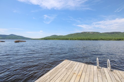 A wooden dock extends into a calm lake, surrounded by green hills under a clear blue sky.