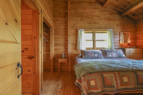 Cozy wooden bedroom with a quilted bed, natural light, and rustic decor, featuring a closet and a small chair.