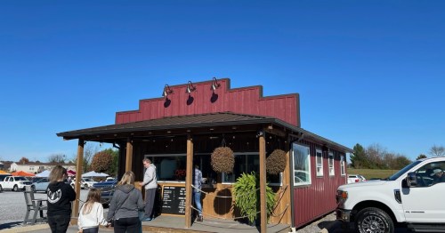 A small red building with a porch, people waiting outside, and a clear blue sky in the background.
