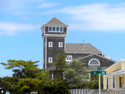 A tall, wooden building with a tower, surrounded by trees, under a blue sky near a street sign for 1st Avenue.