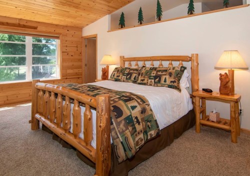 Cozy bedroom with a wooden bed, nature-themed bedding, and warm lighting, featuring a rustic cabin aesthetic.