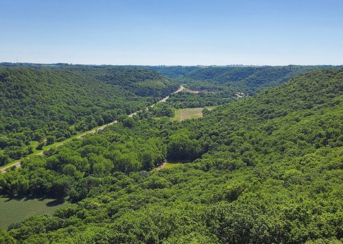 A panoramic view of lush green hills and a winding road through a valley under a clear blue sky.