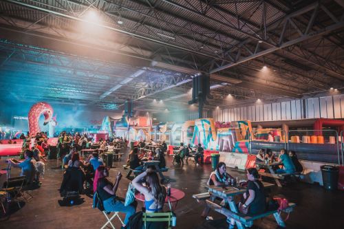 A lively indoor event space with colorful inflatable attractions and people socializing at tables.
