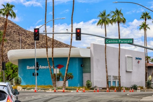 Bank of America building at an intersection with traffic lights and palm trees under a blue sky.