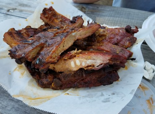 A pile of grilled, smoky ribs on a paper tray, showcasing a rich, caramelized glaze.