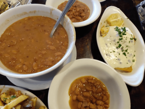 A bowl of refried beans, a plate of cheesy enchiladas, and a small bowl of pinto beans on a wooden table.