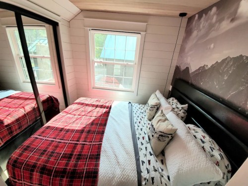 Cozy bedroom with a plaid blanket, decorative pillows, and large windows showcasing a mountain view.
