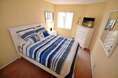 Cozy bedroom with a white bed, blue striped bedding, dresser, TV, and natural light from a window.