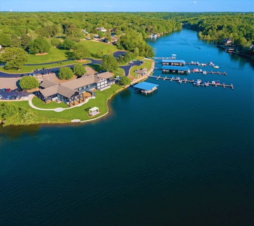 Aerial view of a serene lake with docks, green landscapes, and a residential area along the shore.