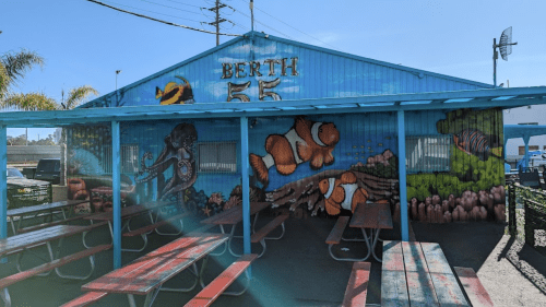 Colorful mural of sea life on a blue building with picnic tables in front, labeled "Berth 55."