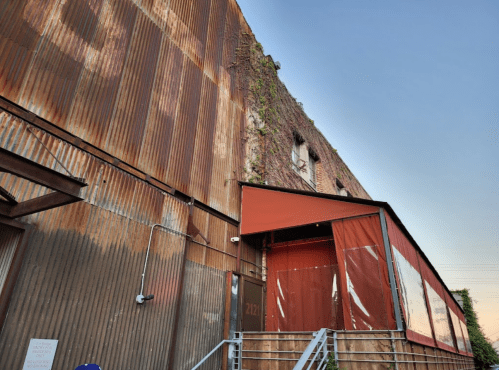 Rusty industrial building with ivy-covered walls and a red awning entrance, under a clear blue sky.