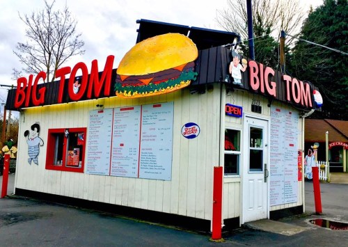 A small fast-food stand named "Big Tom" with a large burger sign, featuring a menu and bright red accents.