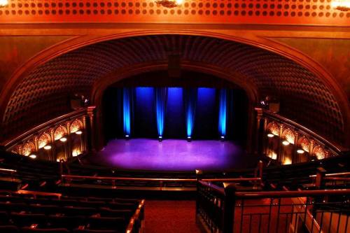 A beautifully lit theater stage with blue curtains and ornate architectural details, viewed from the audience.