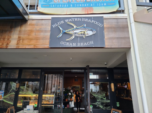 Sign for "Blue Water Seafood" at Ocean Beach, with a fish graphic, above the entrance of a restaurant.
