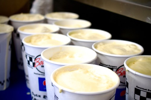 A row of cups filled with creamy ice cream, some with a frothy top, on a blue surface.