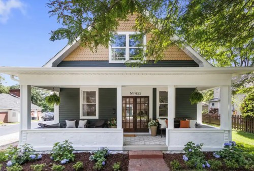 A charming two-story house with a front porch, green siding, and a landscaped garden.