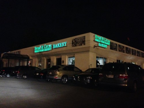 A bakery named "Bread & Circles" illuminated at night, with parked cars in front and a clear sky above.