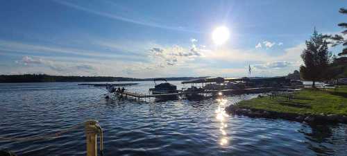 A serene lakeside scene with boats docked, sunlight reflecting on the water, and a clear blue sky.